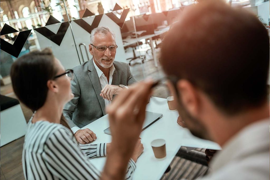 Modernes Büro mit drei Business-Personen die an einem Tisch sitzen und sich austauschen.
